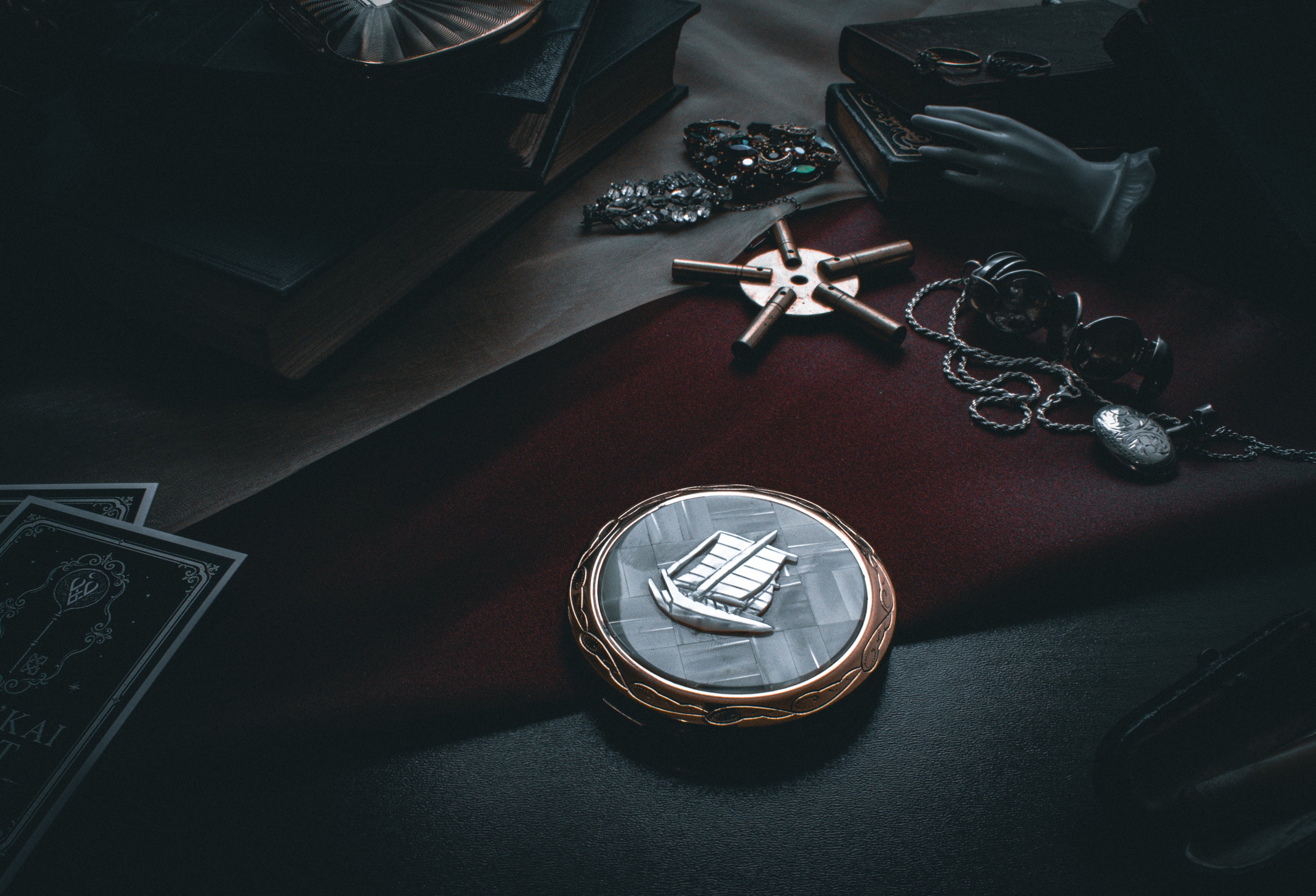 A mother of pearl tie tab in the shape of a sword. The tie tab is sitting on a leather blue book with scattered jewelry around it.