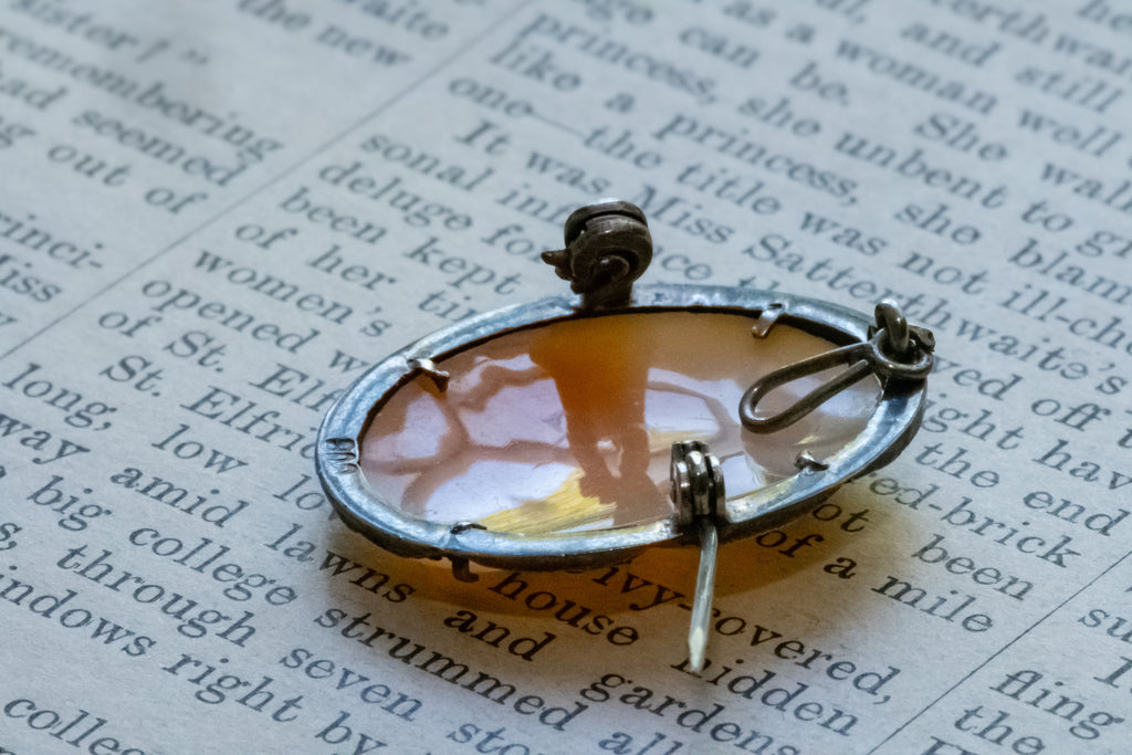 A silver-toned oval pin with a translucent amber-orange center and a small dark metal top, photographed close up on printed book text.