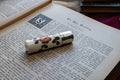 A vintage ceramic scent bottle with a floral pattern and silver-toned metal casing, resting on an open antique book.