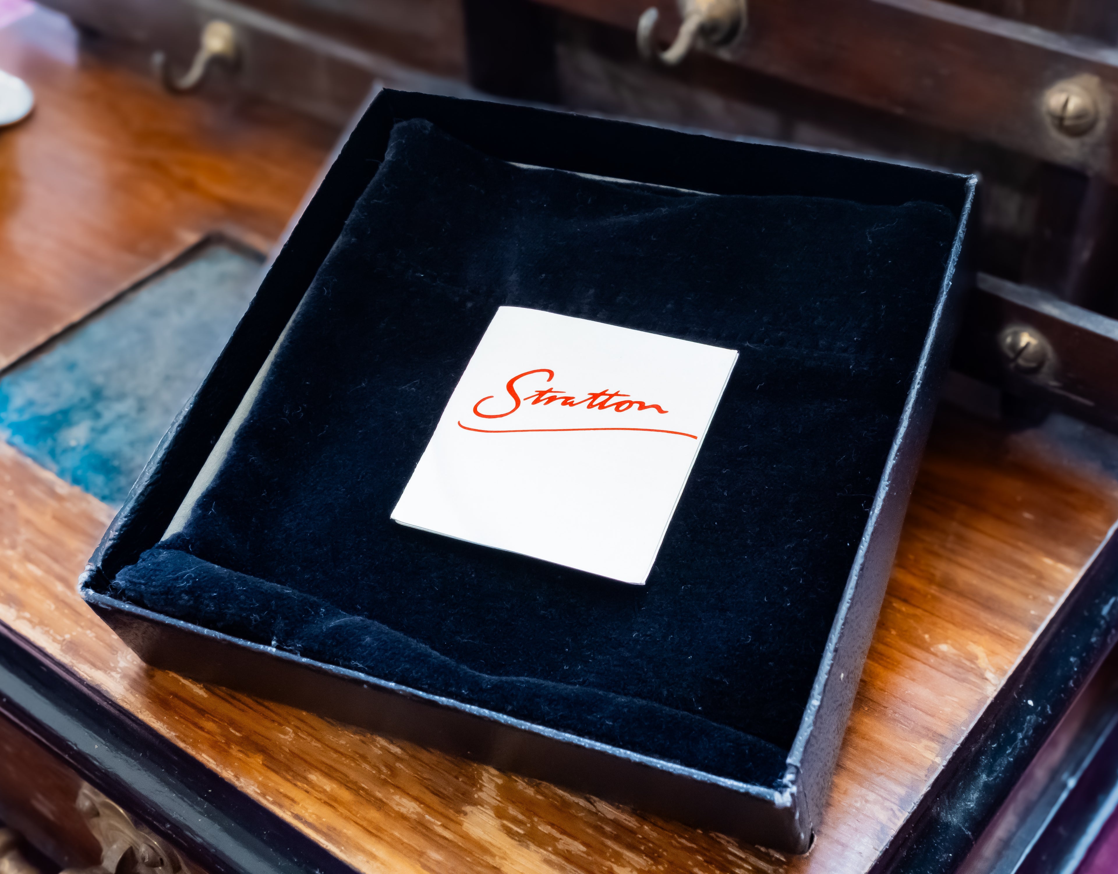 A black presentation box with a black velvet interior, open on a wooden surface. A small white card with the red script brand name 'Station' is placed in the center.