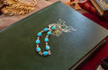 A silver chain bracelet with oval turquoise-blue stones, displayed on a dark green book with gold ornamental detailing.