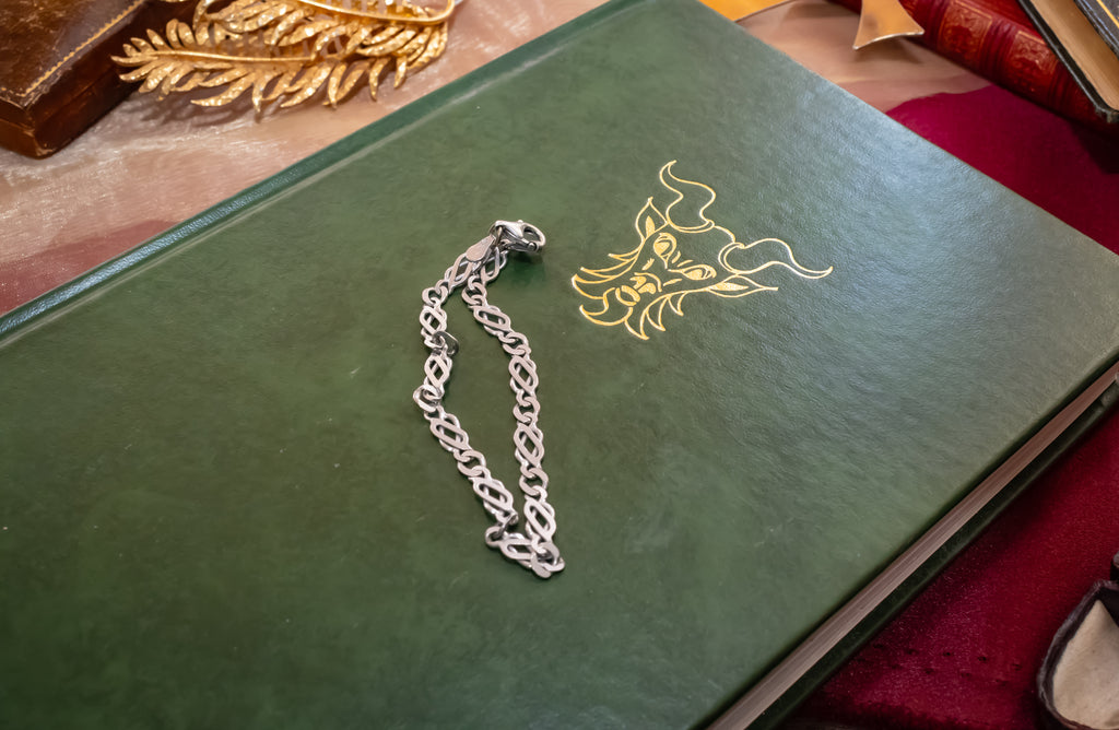 A silver chain accessory with a lobster clasp and decorative link pattern, laid on a dark green book with a gold emblem.
