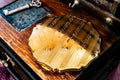 A close-up of an ornate gold compact mirror with engraved vertical stripes and scalloped edges, resting on a vintage wooden box next to a small antique key.