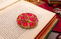 A round enamel Stratton powder compact with a vibrant pink rose floral pattern and gold scalloped edges, resting on an open vintage book.