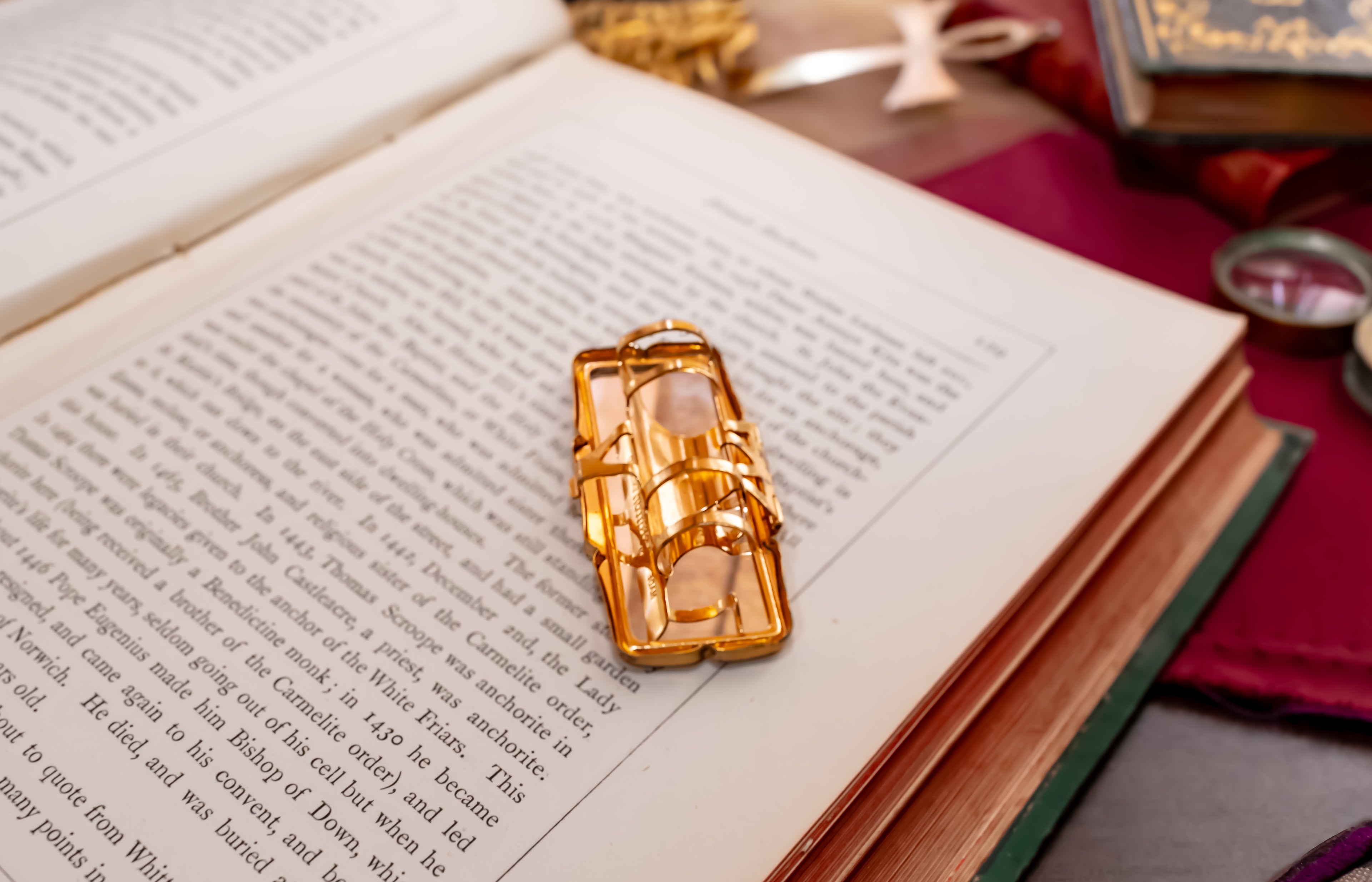 A gold-toned Stratton lipstick holder with a mirror  with a detailed illustration of Santa Claus sitting on a book, resting on an open book with printed text.