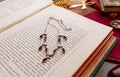 A silver-toned pendant necklace with multiple teardrop-shaped dark red gemstones and small white pearl accents, displayed on an open book with vintage props around it.