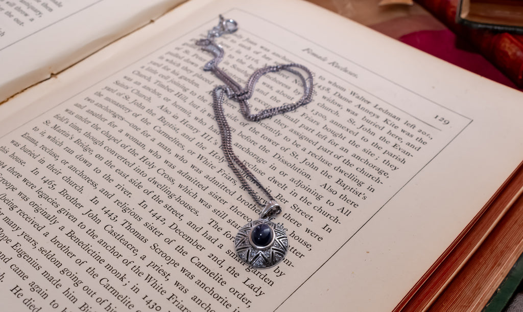 A silver-toned chain necklace with a circular pendant featuring a central black stone, laid across the pages of an open book.