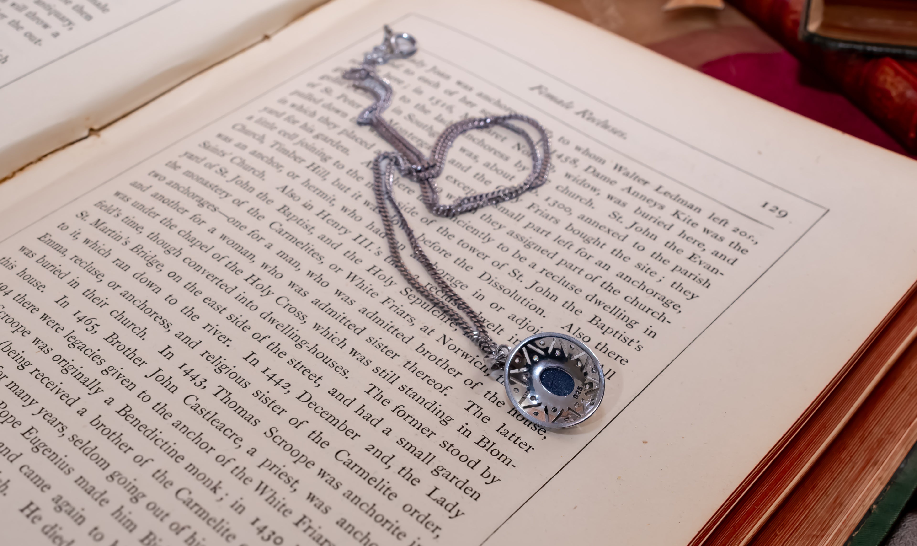 A silver-toned chain necklace with a circular pendant featuring a blue center and white border, resting on an open book with printed text.