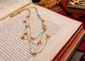 A gold-toned layered necklace with multiple heart-shaped charms draped over an open book, surrounded by vintage books and a gold decorative object.