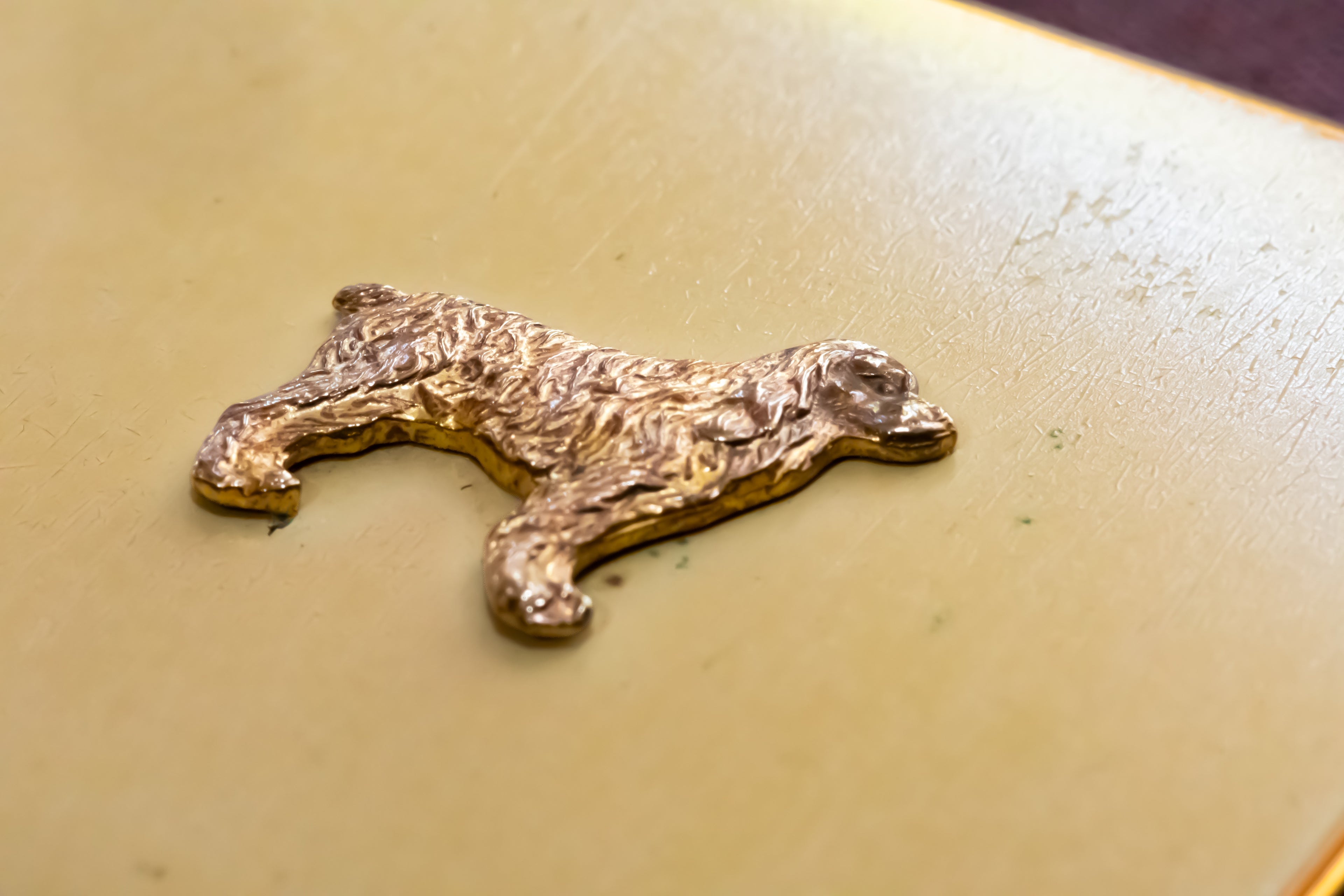 A small metallic gold dog-shaped ornament or charm resting on a textured beige surface.