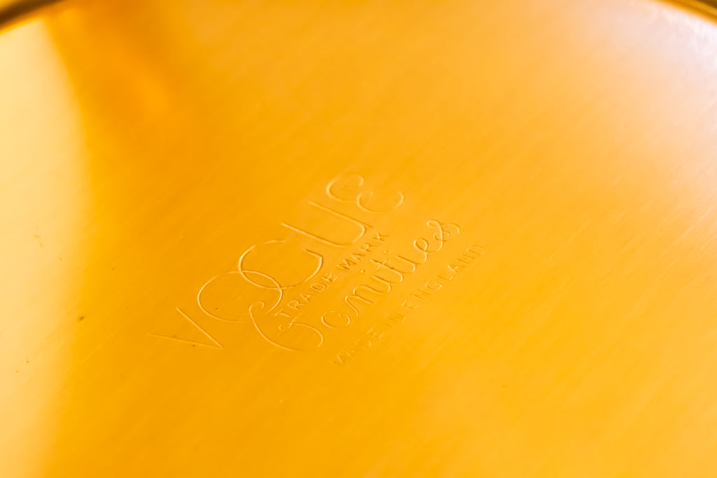 Close-up of a yellow-gold metallic surface with an embossed Vogue logo in the center.