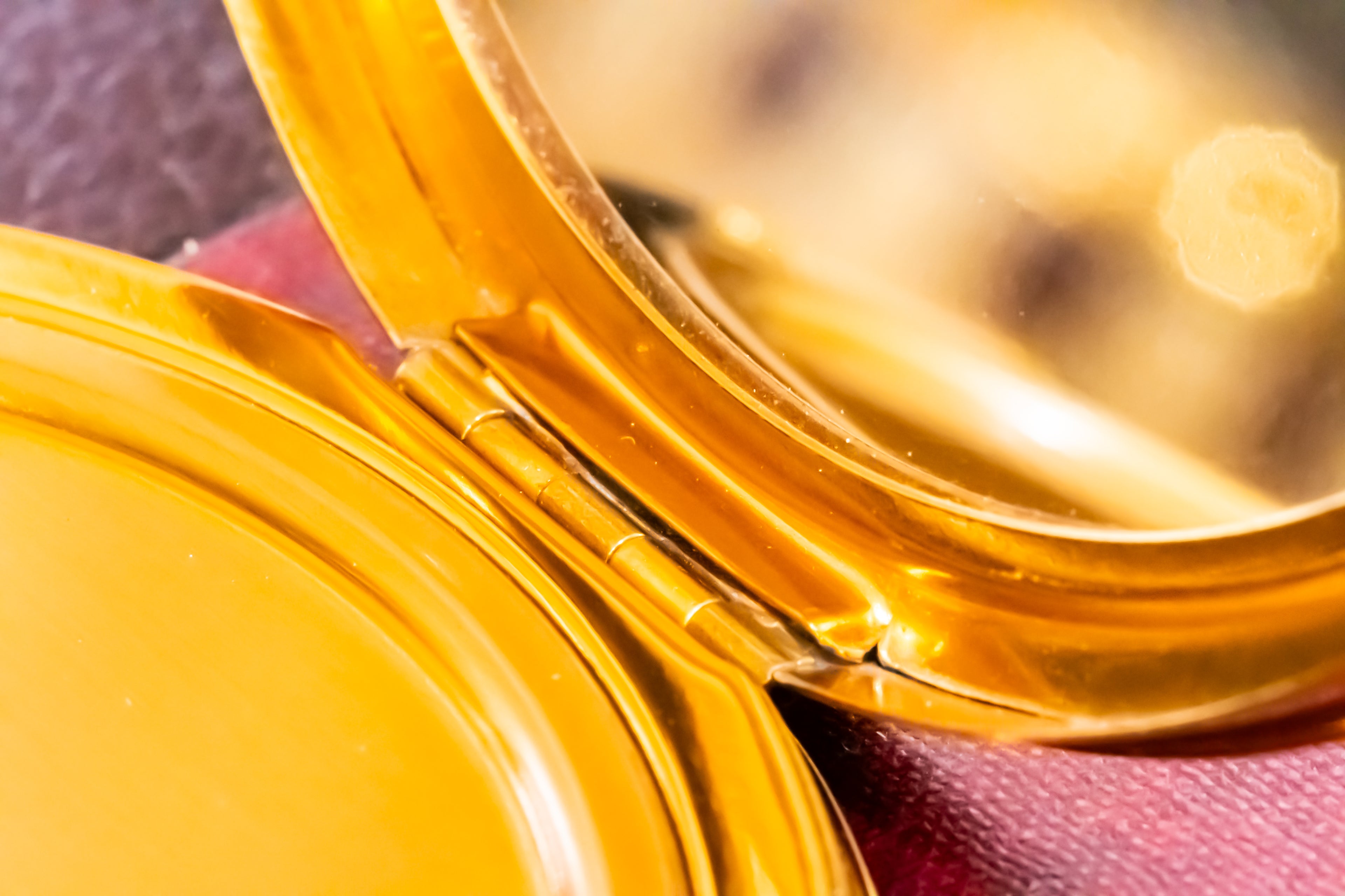 Close-up of an open round gold compact case with a mirror inside, resting on a textured burgundy surface.