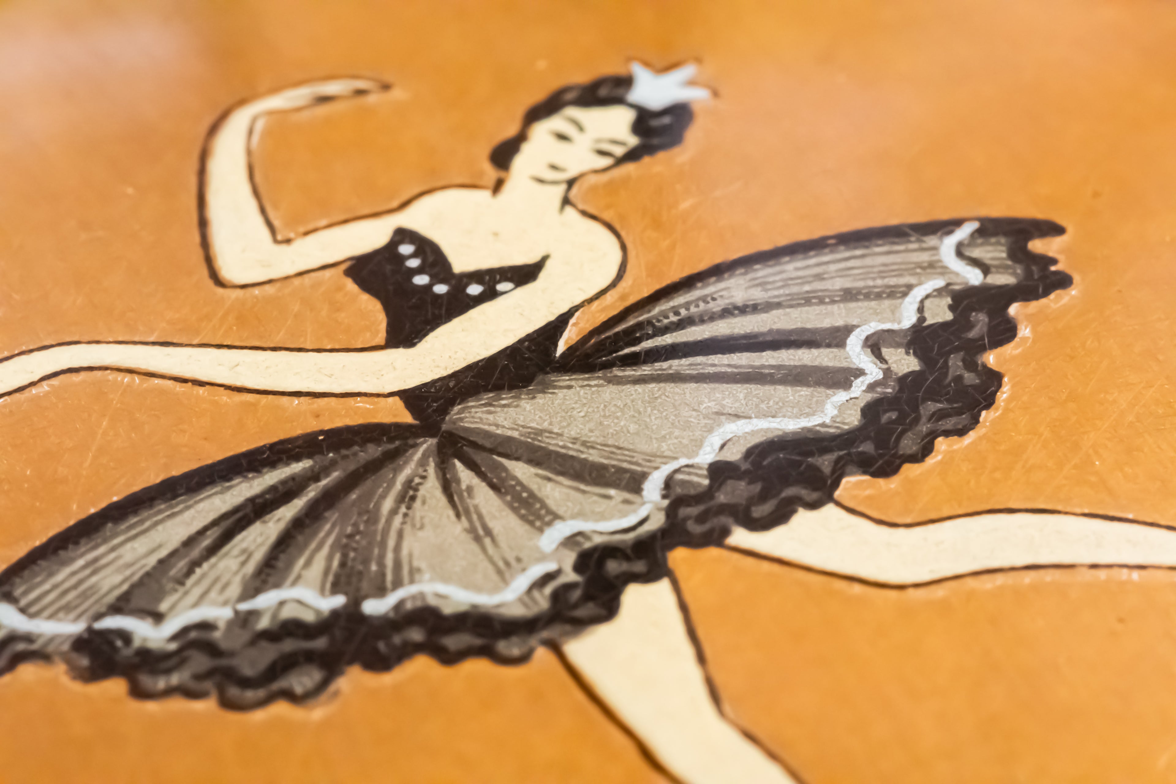 A close-up of a vintage-style illustration of a ballerina in a black tutu against a warm orange-brown background.