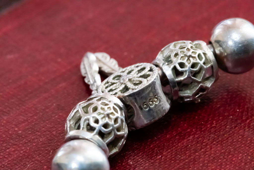 A close-up of silver filigree and bead jewelry components on a textured red surface, with one section stamped '999'.