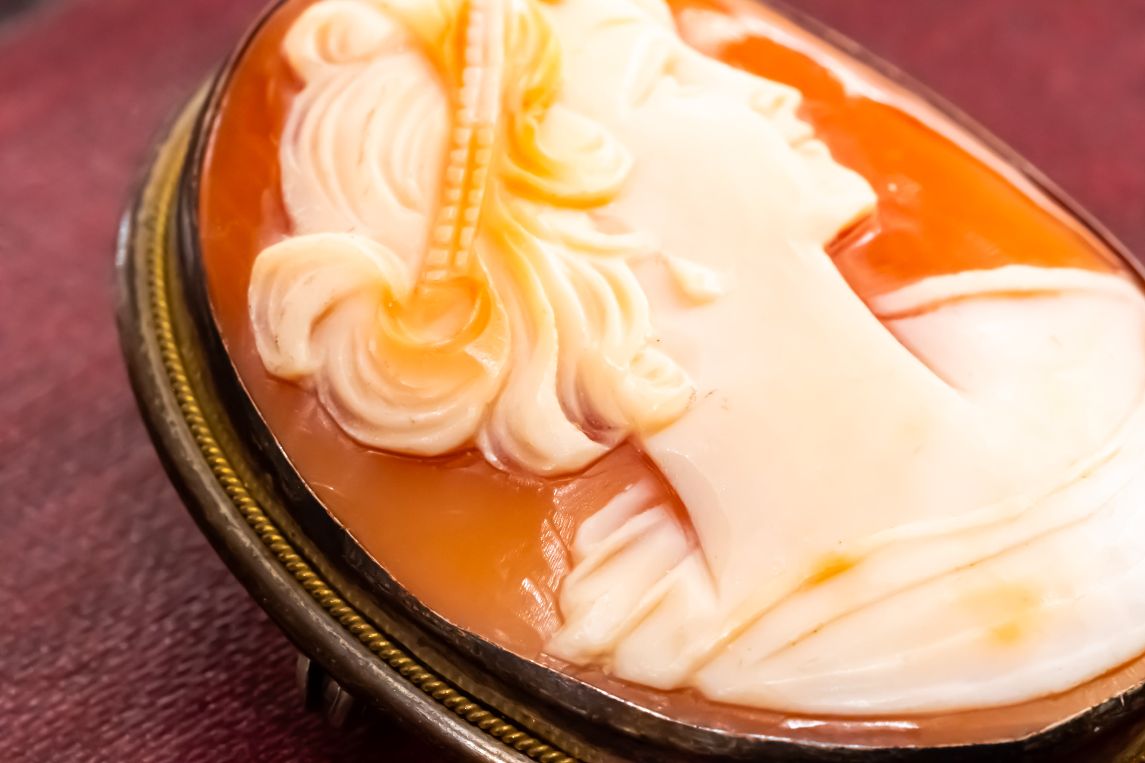 An antique-style carved cameo oval brooch featuring a profile portrait of a woman with flowing hair, set in amber-brown resin with a dark metal rim.