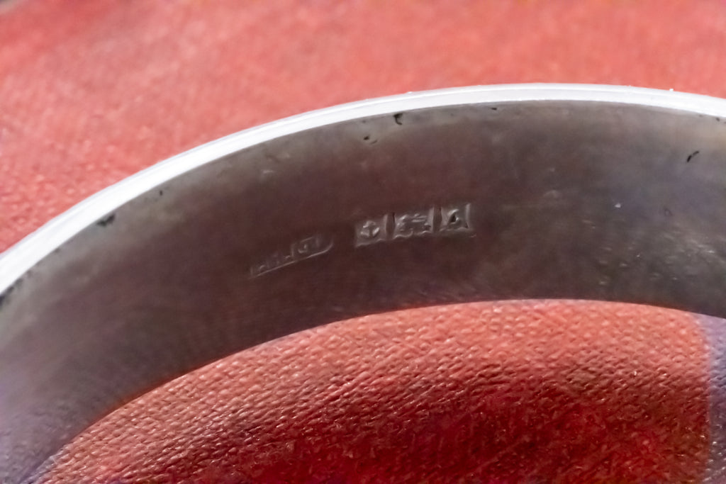 Close-up of the inside of a silver-toned metal bangle bracelet showing sterling silver purity stamps, resting on a textured red surface.