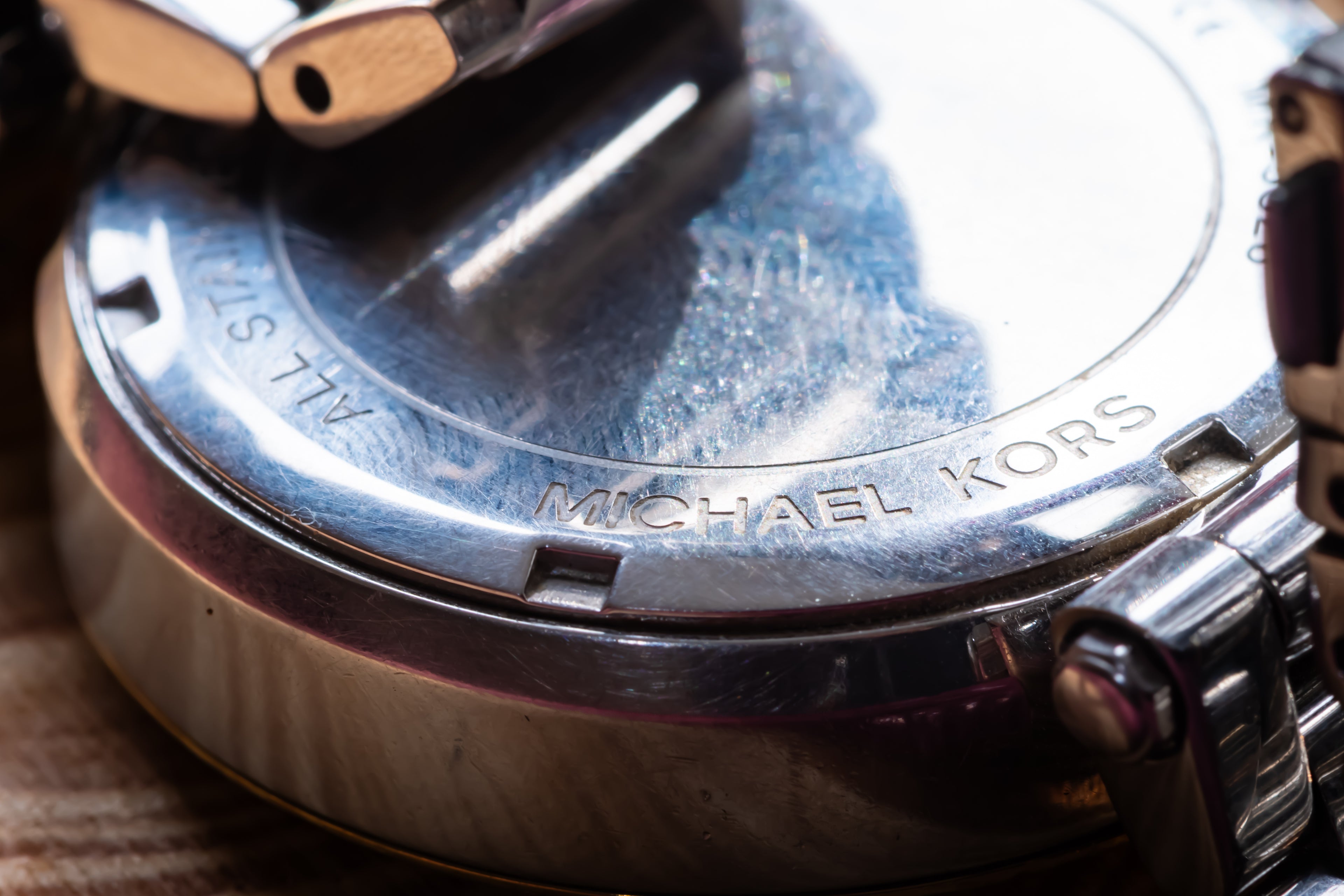 Close-up of the back of a Michael Kors watch case, showing engraved branding and a polished metallic finish with reflections.