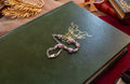 A silver-toned chain bracelet with square purple gemstones rests on the cover of a dark green book with gold foil detailing.