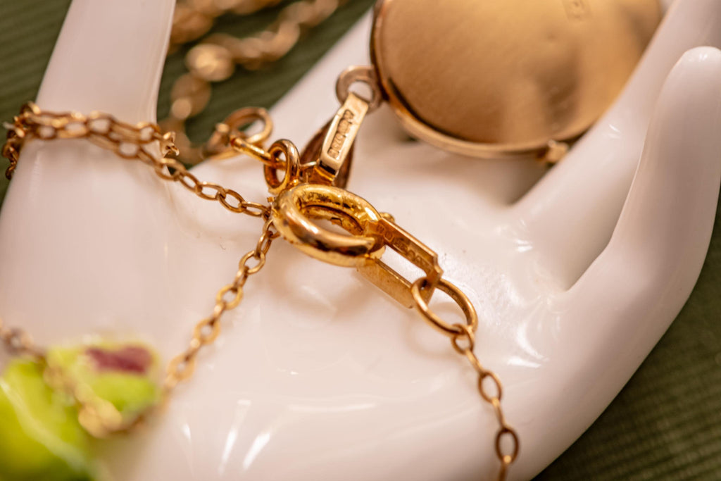 A gold locket attached to a gold chain in a close up picture.