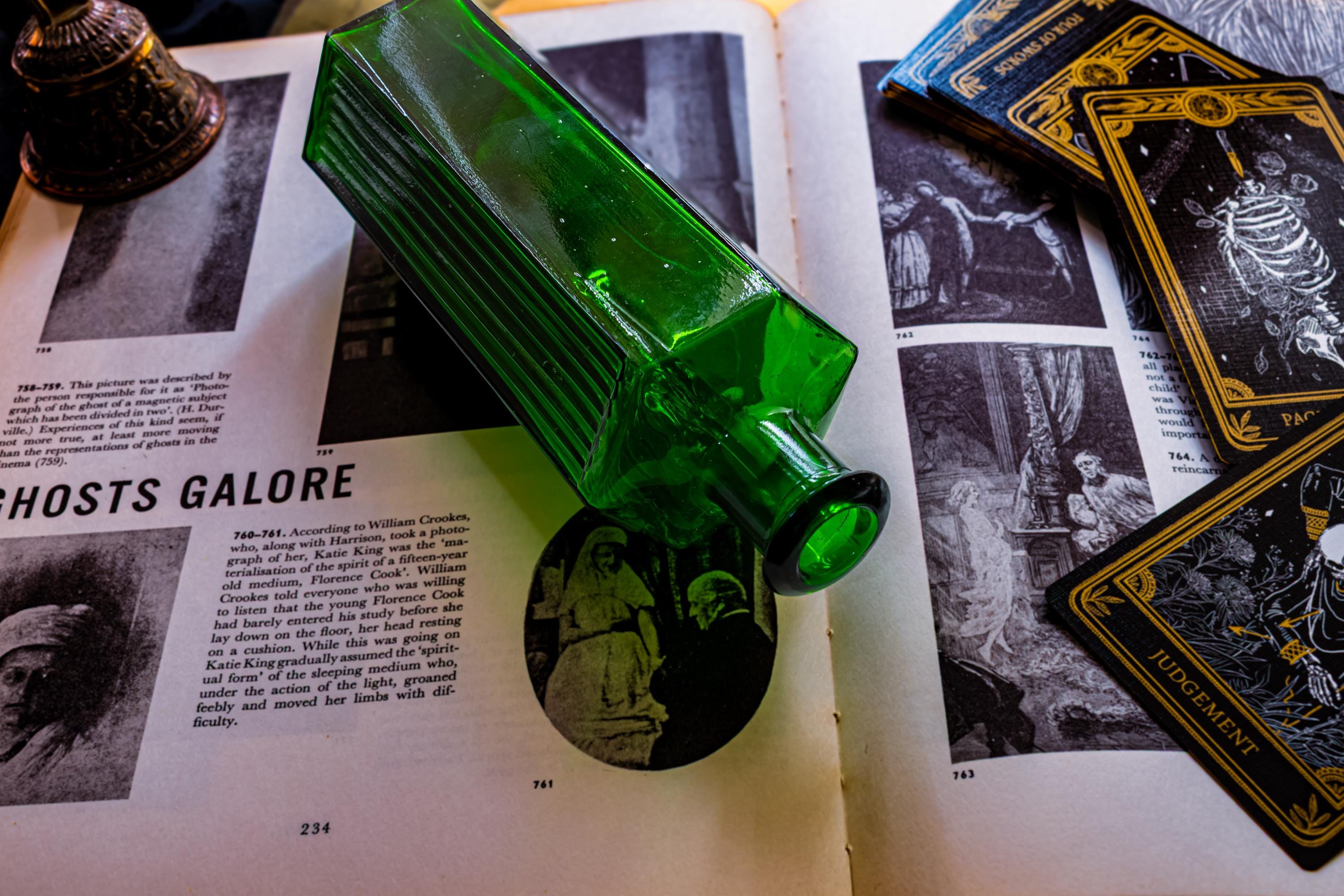 Antique green ribbed glass poison bottle on top of a dark vintage book