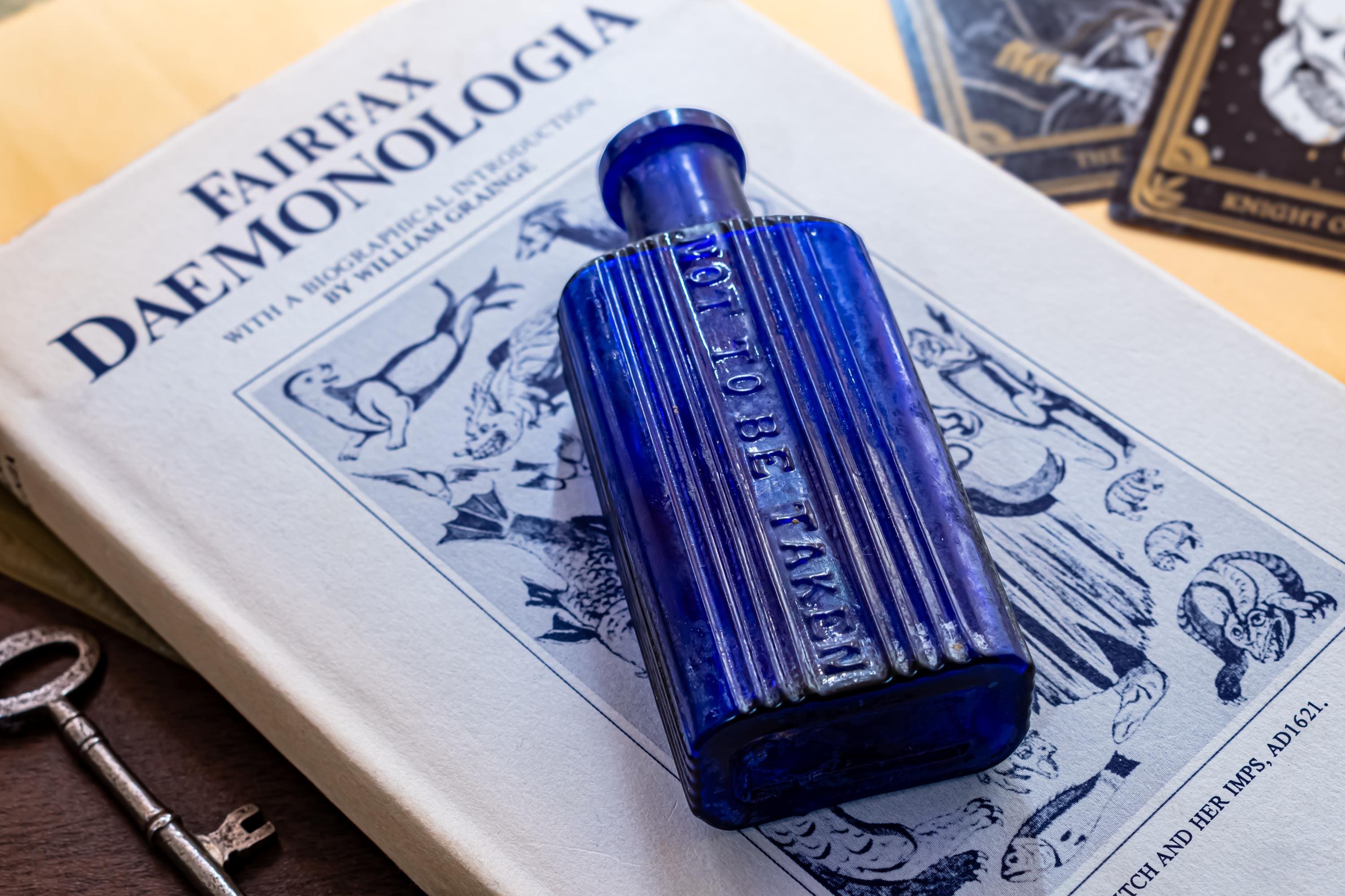Antique cobalt blue ribbed glass poison bottle on top of a dark vintage book