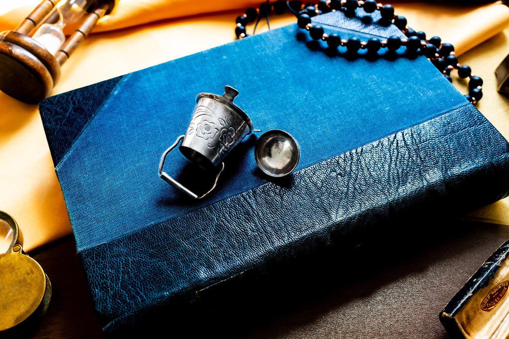 An image showing the side of a Miniature antique silver pail with a small handle, sitting on top of a dark blue vintage book.