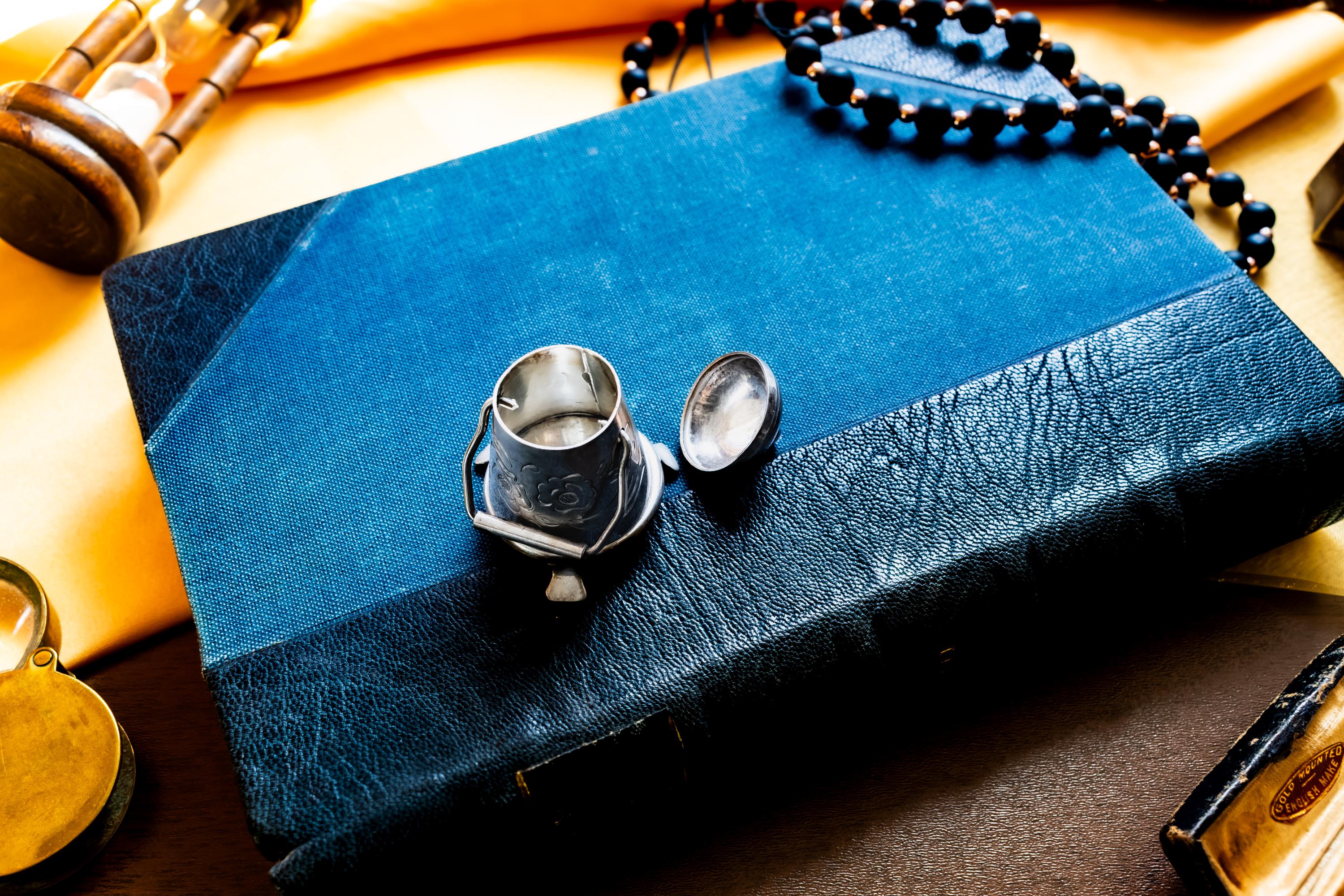 Miniature antique silver pail with a small handle, sitting on top of a dark blue vintage book.