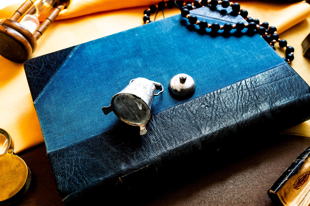 The bottom of a Miniature antique silver pail with a small handle, sitting on top of a dark blue vintage book.