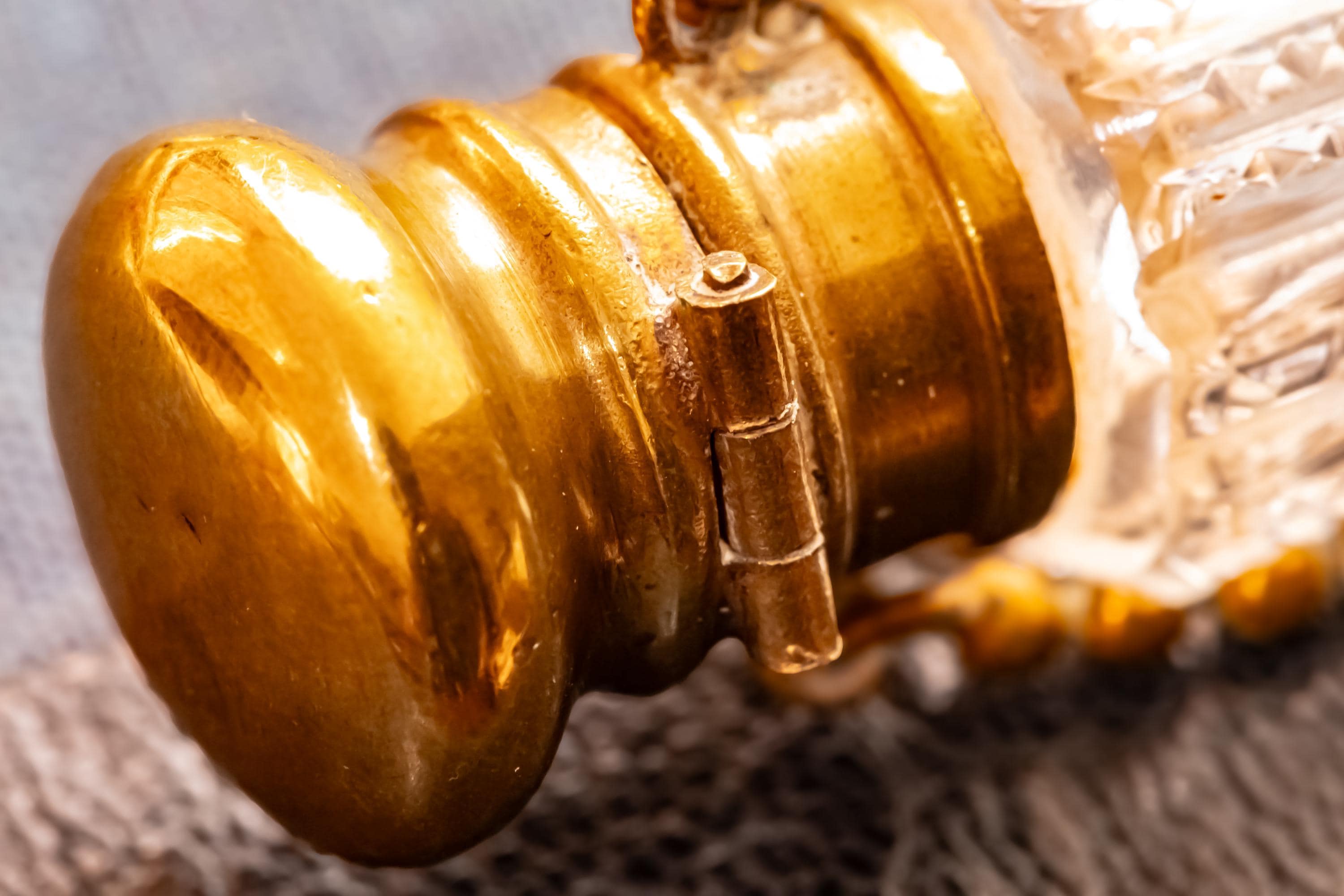 Close up of the top of an Antique crystal horn-shaped perfume vial with brass detailing, attached to a chain and resting on a blue book.