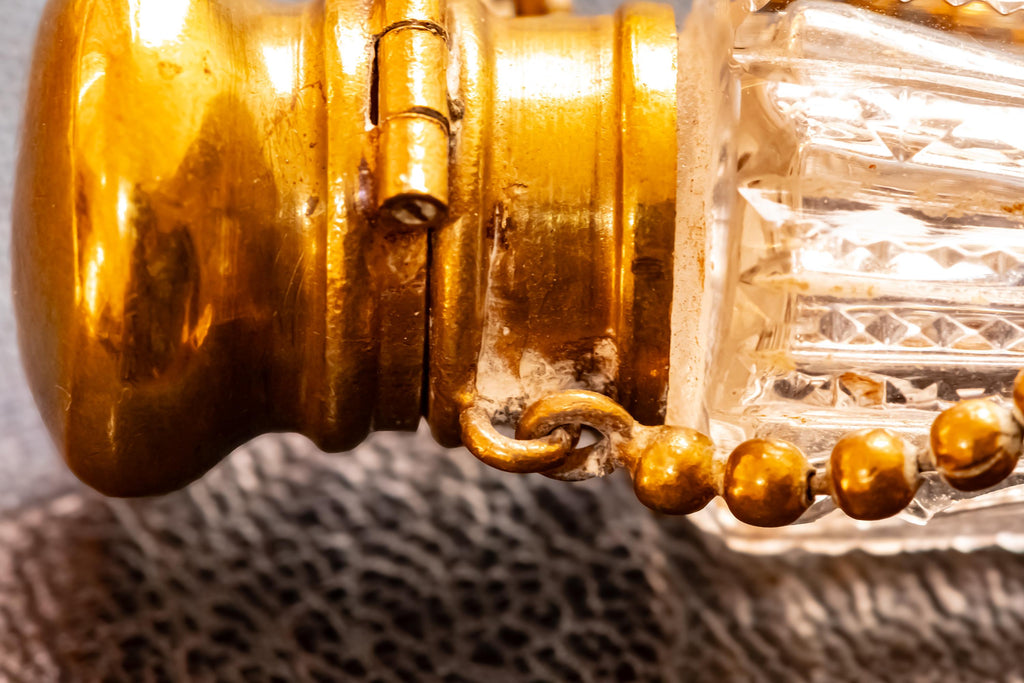 Close up of the top of an Antique crystal horn-shaped perfume vial with brass detailing, attached to a chain and resting on a blue book.
