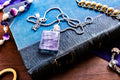 Close-up of a large, rectangular Kunzite gemstone pendant with natural pink and violet banding, set in 925 sterling silver and resting on a textured blue book.