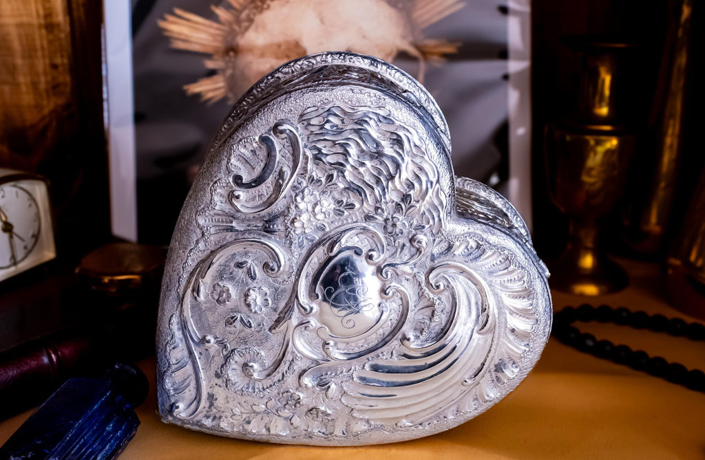 A solid sterling silver hand engraved jewelry box. The shape of the jewelry box is a hard. The box is laying on its side to showcase the engravings of the lid.