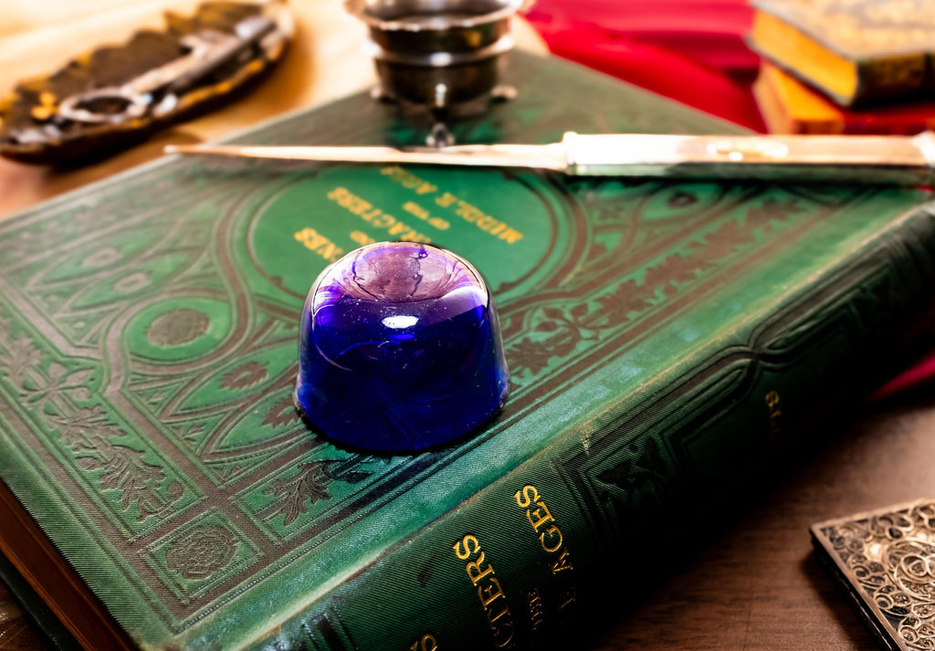 Image showing the bottom of cobalt blue liner of Antique footed silver master salt cellar, resting on top of an ornate green vintage book.