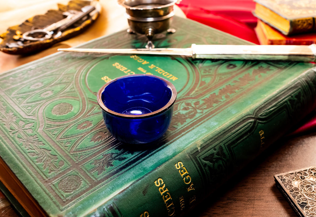 Image showing the cobalt blue liner of Antique footed silver master salt cellar, resting on top of an ornate green vintage book.