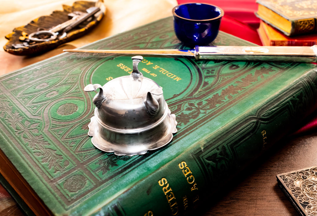 Image showing the bottom of Antique footed silver master salt cellar containing a vibrant cobalt blue glass liner, resting on top of an ornate green vintage book.