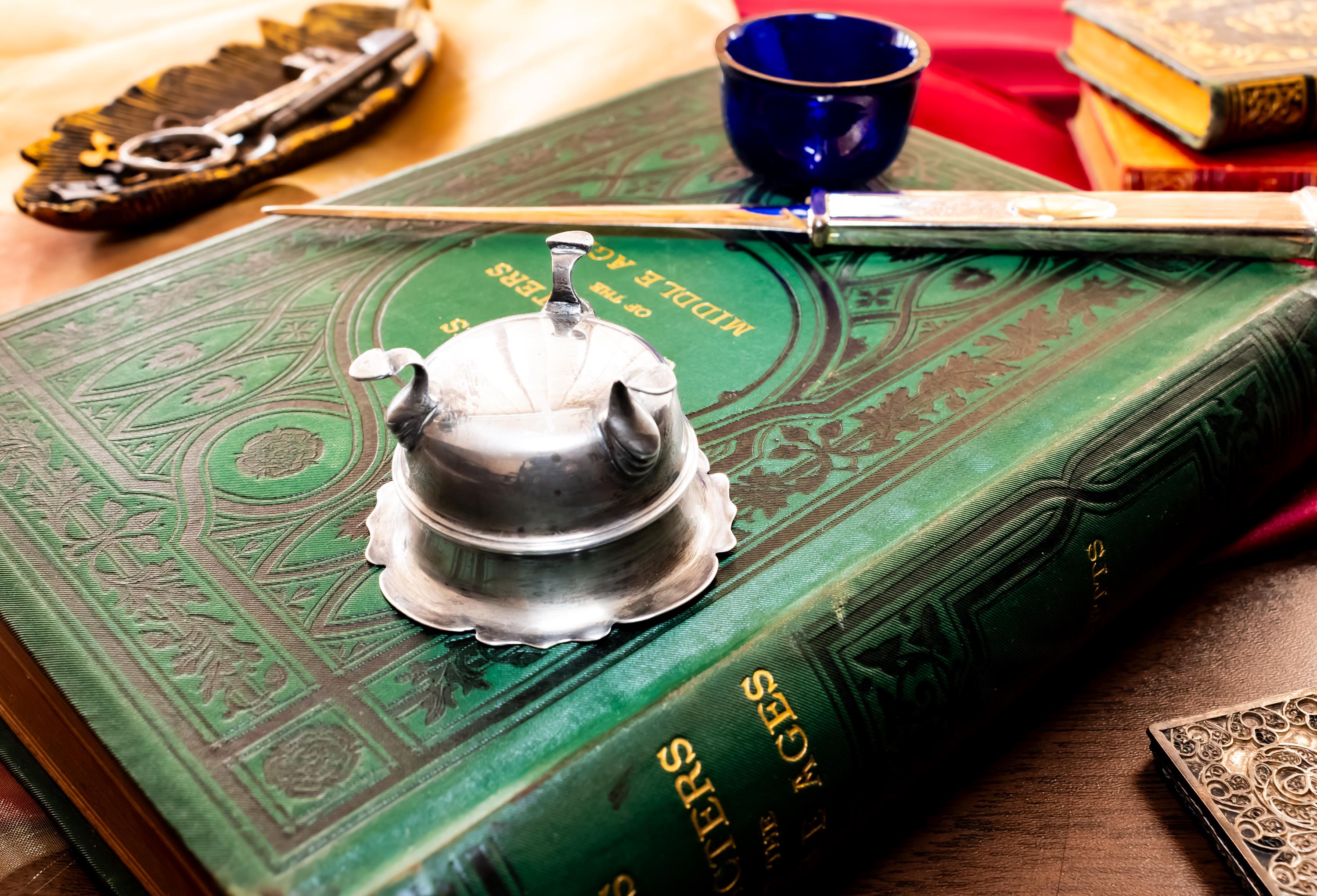 Image showing the bottom of Antique footed silver master salt cellar containing a vibrant cobalt blue glass liner, resting on top of an ornate green vintage book.