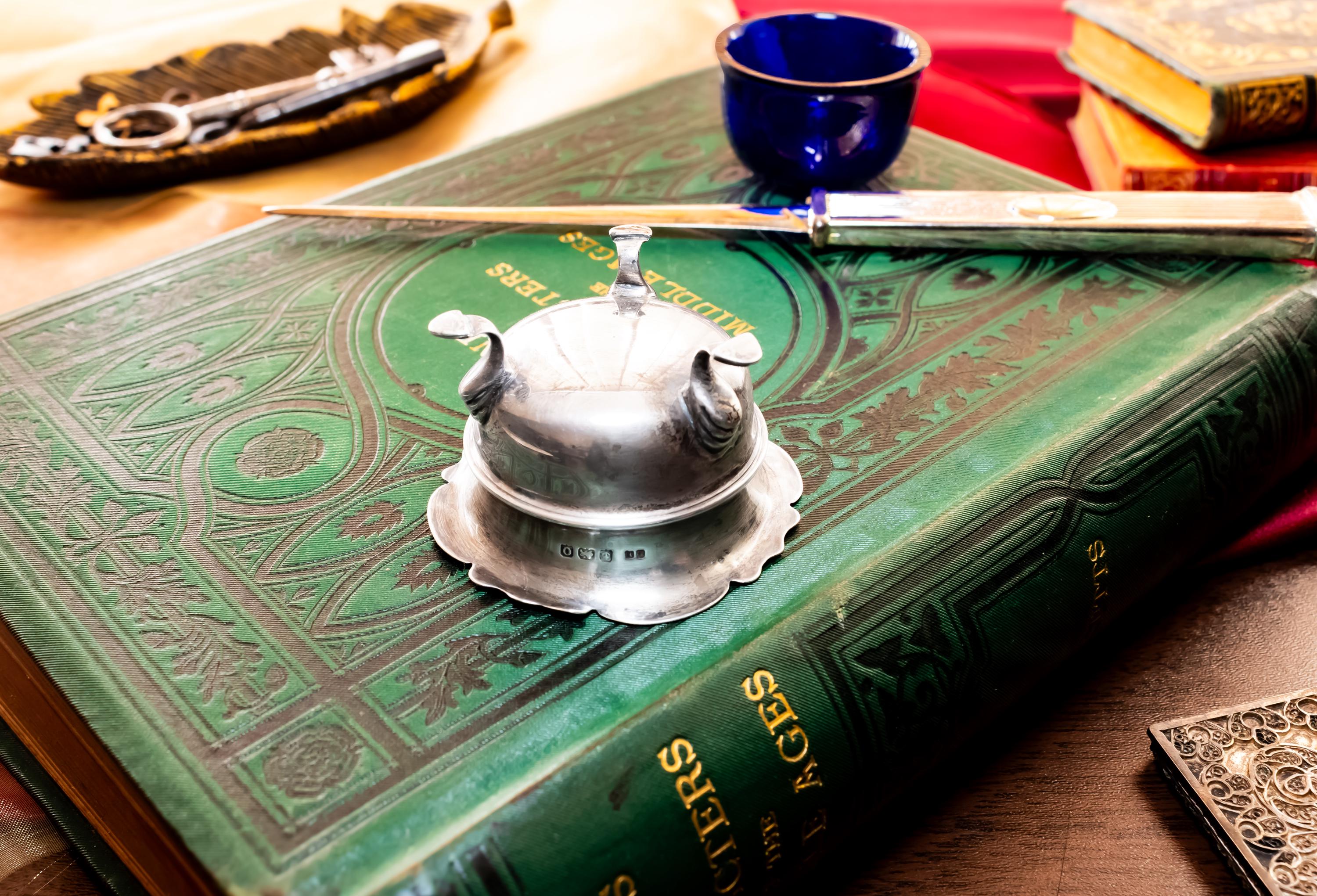 Image showing the bottom of Antique footed silver master salt cellar containing a vibrant cobalt blue glass liner, resting on top of an ornate green vintage book.