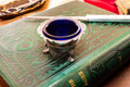 Antique footed silver master salt cellar containing a vibrant cobalt blue glass liner, resting on top of an ornate green vintage book.