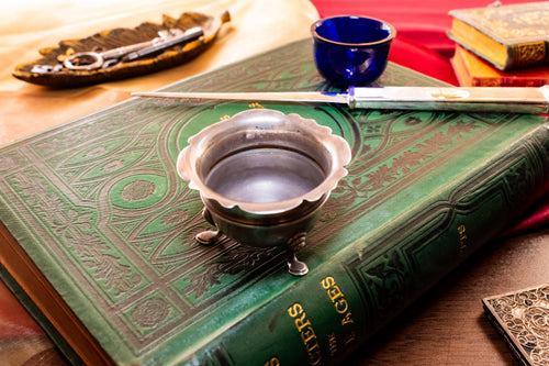 The inside of the Antique footed silver master salt cellar containing a vibrant cobalt blue glass liner, resting on top of an ornate green vintage book.