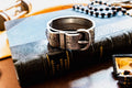Chunky antique silver Victorian hinged bangle bracelet shaped like a buckled belt with floral engravings, resting on a dark vintage book titled Diamonds and Precious Stones.