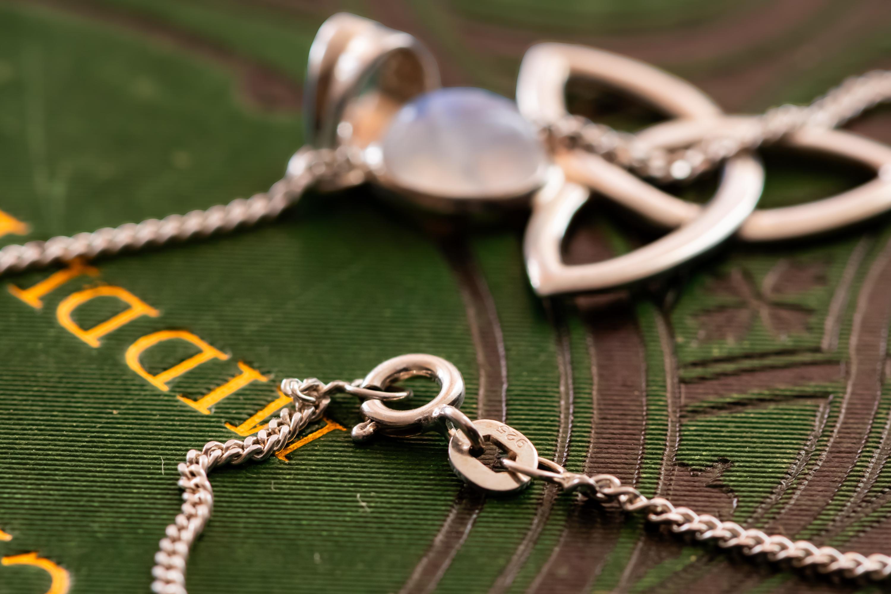 Close-up of a vintage 925 sterling silver pendant necklace featuring a Celtic triquetra knot and a glowing oval moonstone cabochon, resting elegantly on a dark green book cover with gold lettering