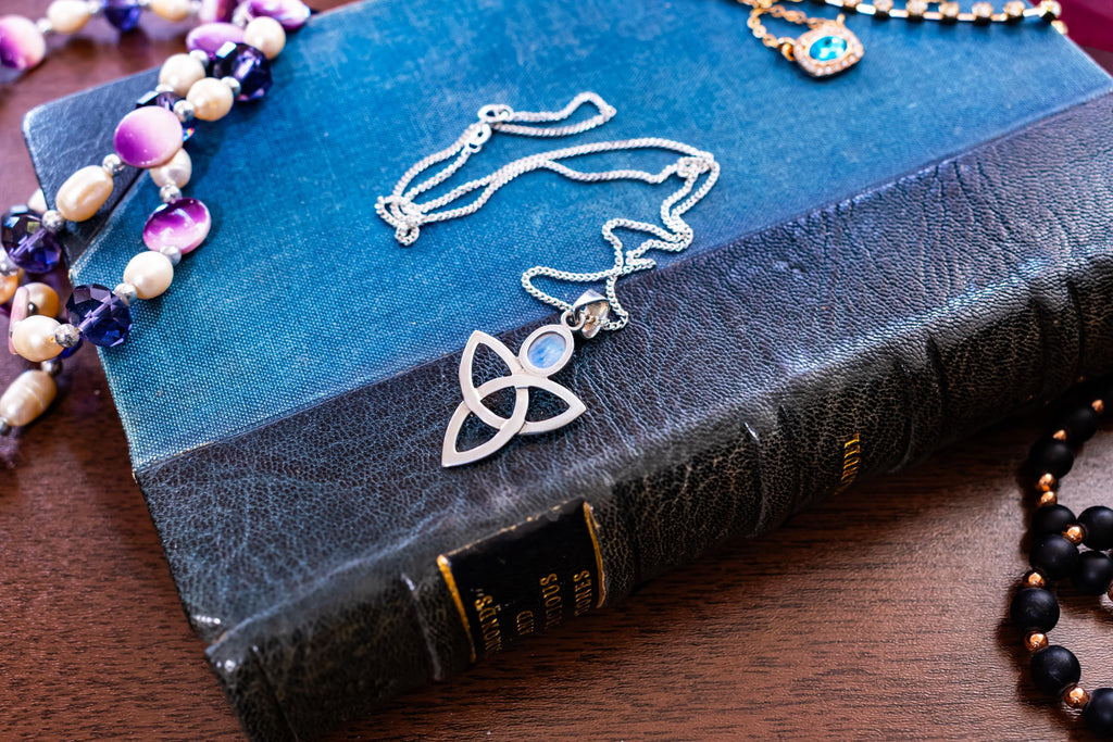 a vintage 925 sterling silver pendant necklace featuring a Celtic triquetra knot and a glowing oval moonstone cabochon, resting elegantly on a blue book cover.