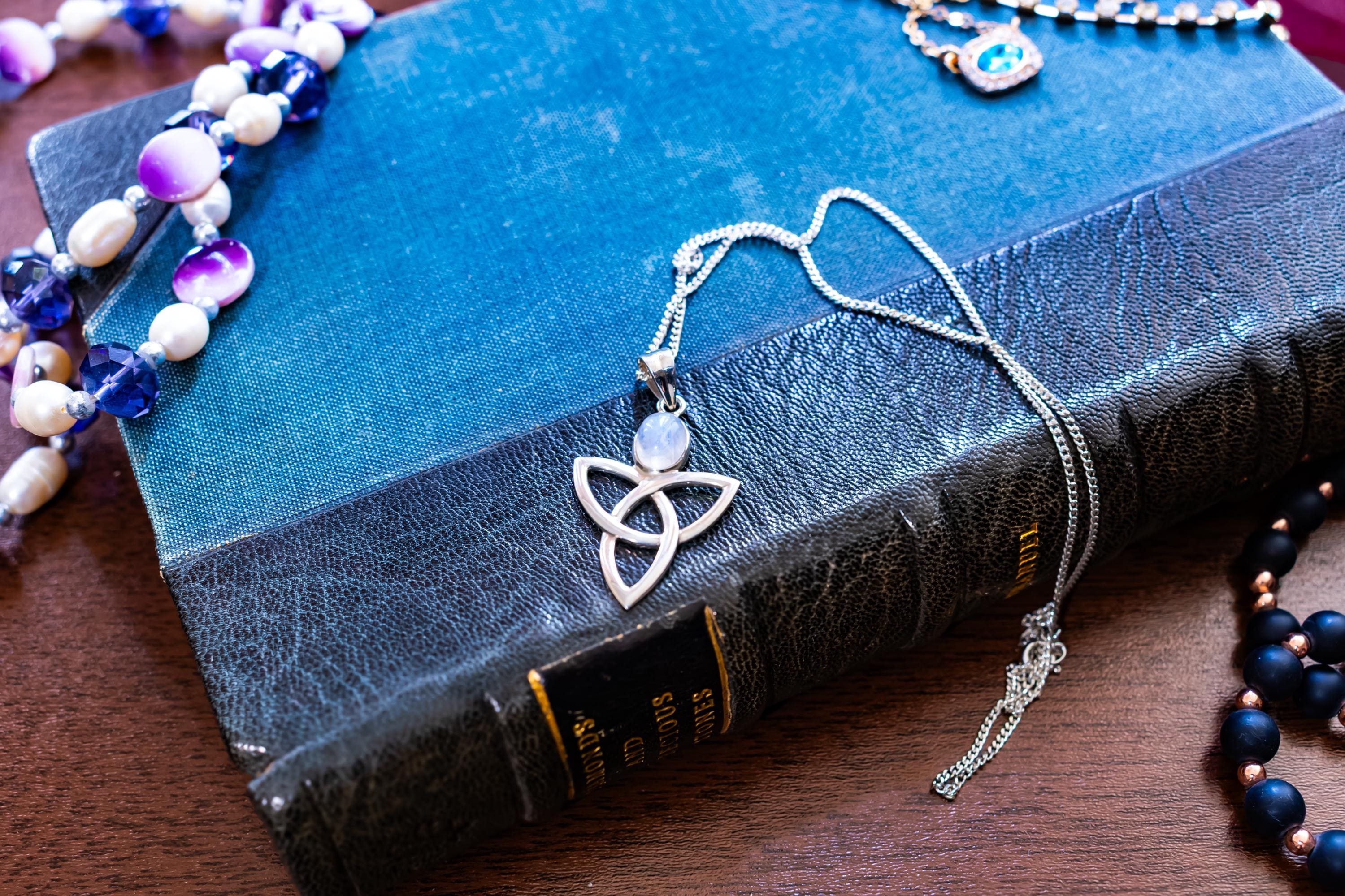 a vintage 925 sterling silver pendant necklace featuring a Celtic triquetra knot and a glowing oval moonstone cabochon, resting elegantly on a blue book cover.