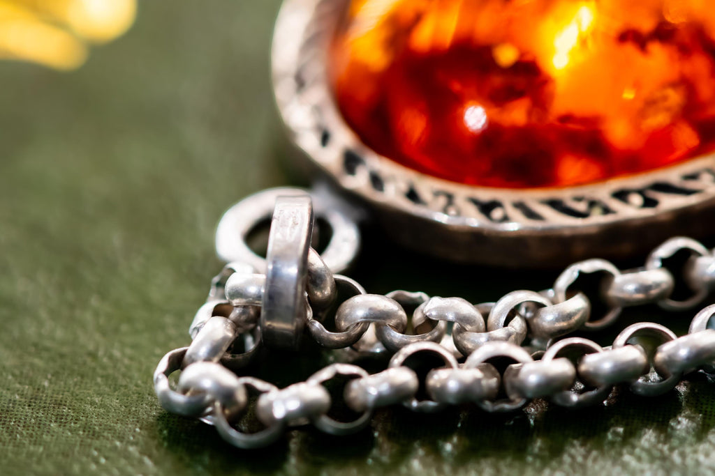 Close-up of a vintage 925 sterling silver necklace featuring a polished oval Baltic amber cabochon with a twisted silver rope border, resting on a dark green book with gold foil detailing