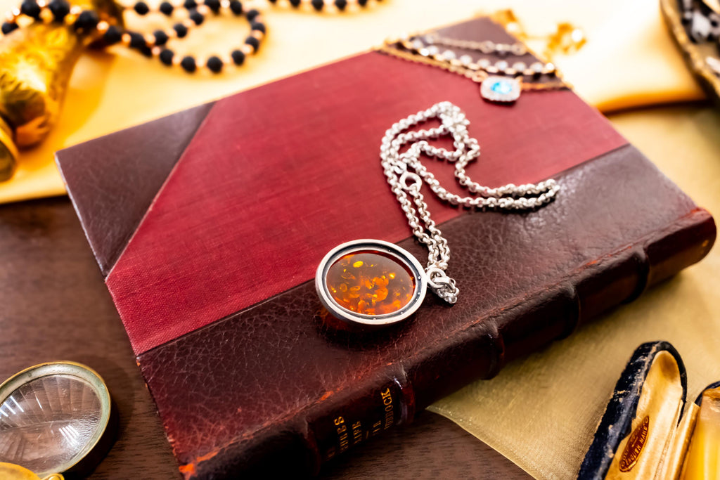 a vintage 925 sterling silver necklace featuring a polished oval Baltic amber cabochon with a twisted silver rope border, resting on a dark red book.