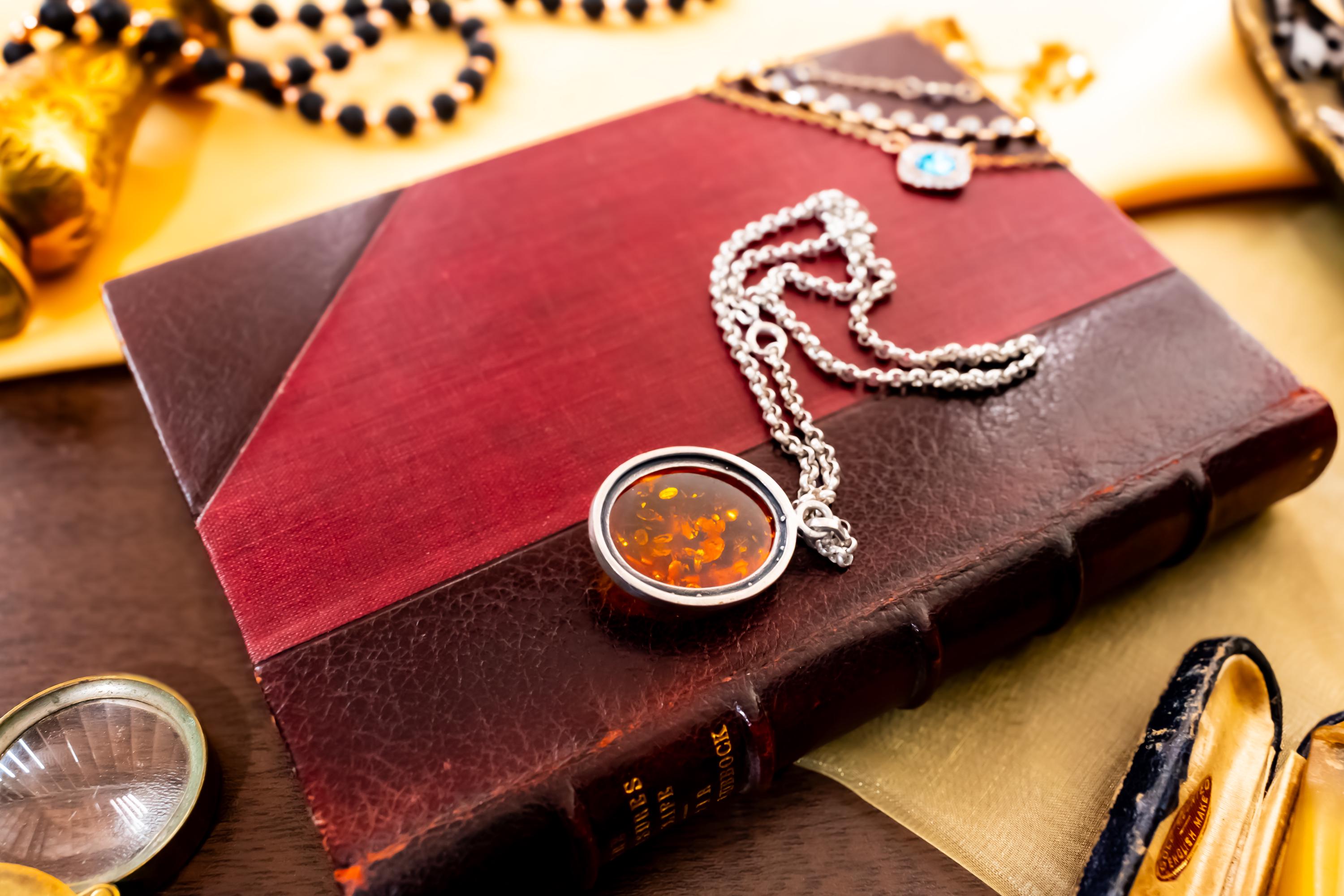 a vintage 925 sterling silver necklace featuring a polished oval Baltic amber cabochon with a twisted silver rope border, resting on a dark red book.