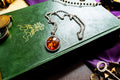 a vintage 925 sterling silver necklace featuring a polished oval Baltic amber cabochon with a twisted silver rope border, resting on a dark green book with gold foil detailing