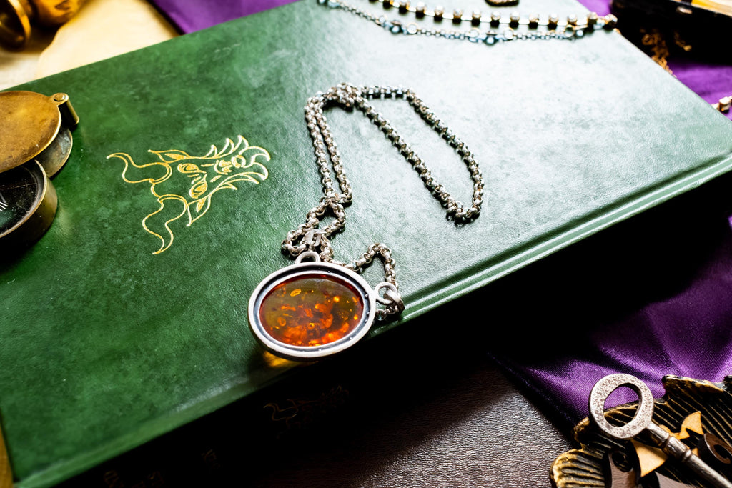 a vintage 925 sterling silver necklace featuring a polished oval Baltic amber cabochon with a twisted silver rope border, resting on a dark green book with gold foil detailing