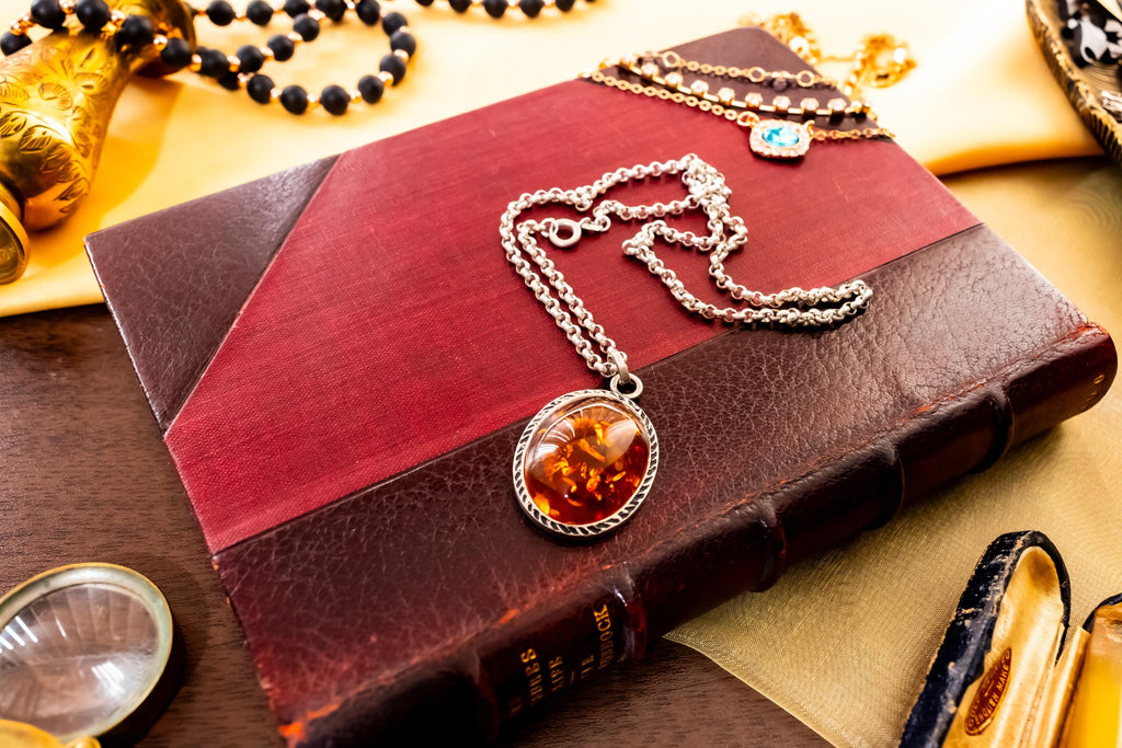 a vintage 925 sterling silver necklace featuring a polished oval Baltic amber cabochon with a twisted silver rope border, resting on a dark red book.