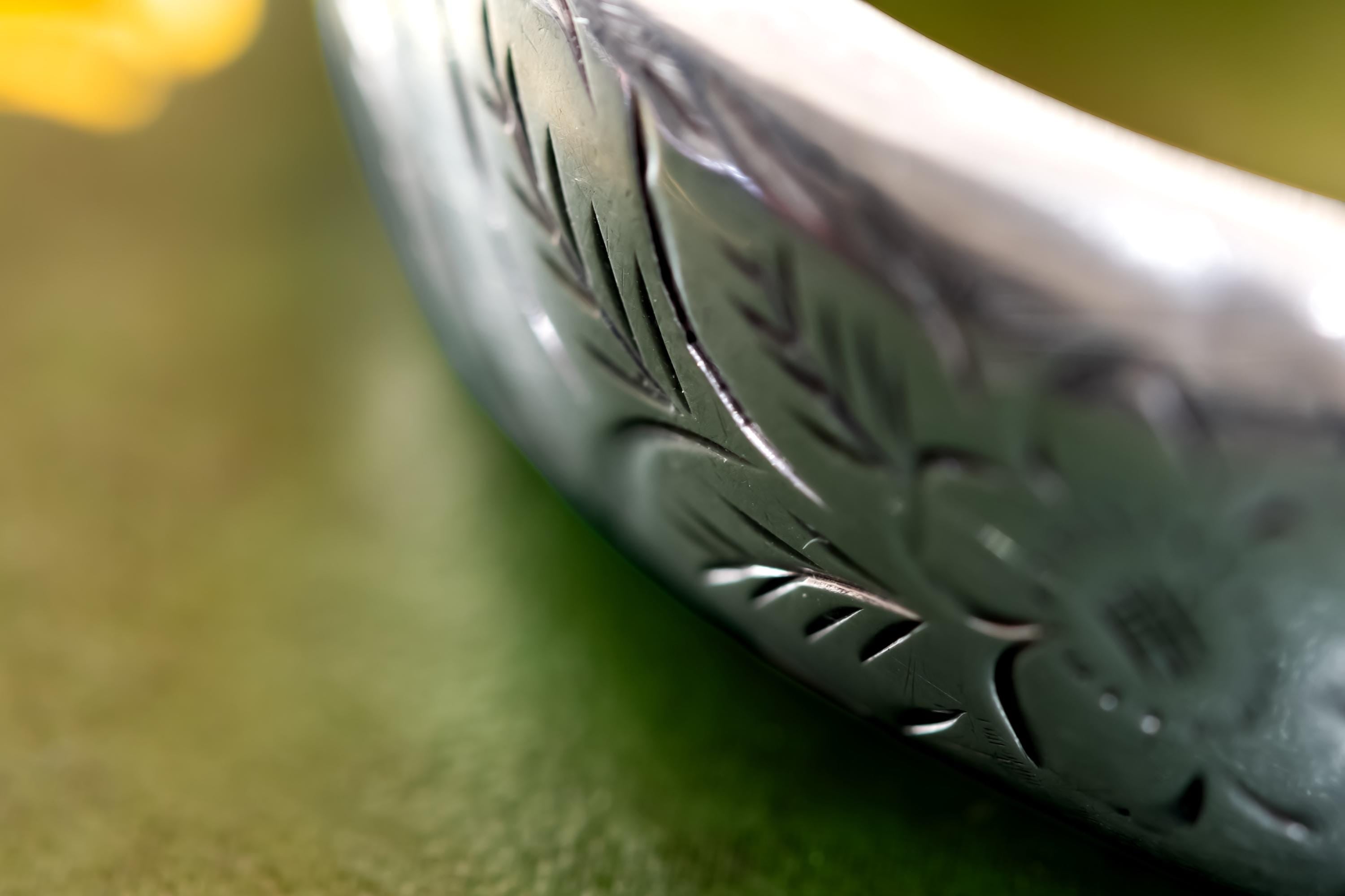 Close-up of a wide, vintage 1969 Birmingham sterling silver hinged bangle with intricate botanical engravings and a safety chain, resting beautifully on a vintage leather-bound book.